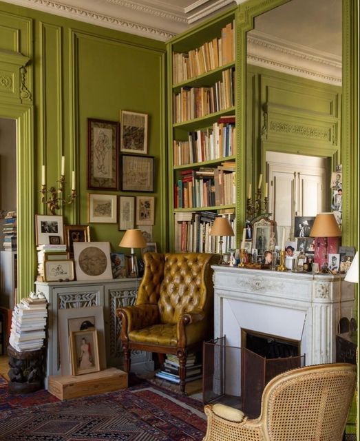 an exquisite living room with chartreuse walls, a leather and cane chair, a fireplace, an oversized mirror and shelves