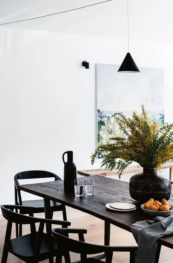 an exquisite modern dining space with a dark-stained reclaimed table and black chairs, a pendant lamp and some blooms