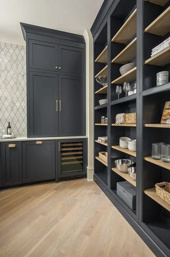 an exquisite soot pantry with built in cabinets and shelves, gold handles and baskets plus a tiled wall is a lovely and cool space