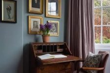an exquisite vintage working nook with grey walls, a vintage dark-stained bureau and a mauve chair, mauve curtains and a gallery wall