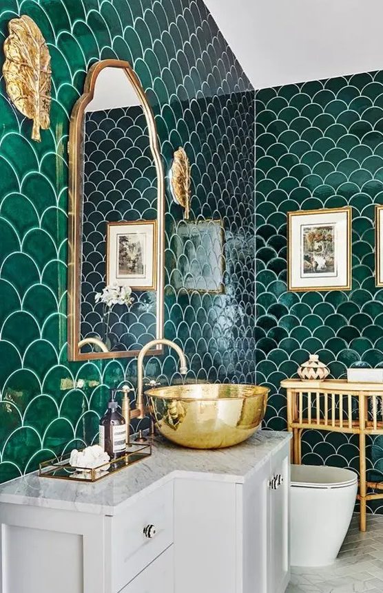 an extra bold bathroom clad with emerald fishscale tiles, gold fixtures and a sink and a neutral floor and vanity to calm down the space