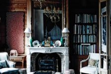 an eye-catchy Goth living room with burgundy walls, bookcases, a fireplace, a vintage chandelier and floral seating furniture