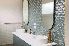 an eye-catchy bathroom clad with white tiles and grey green fishscale tiles plus a matching vanity, sinks and gold fixtures