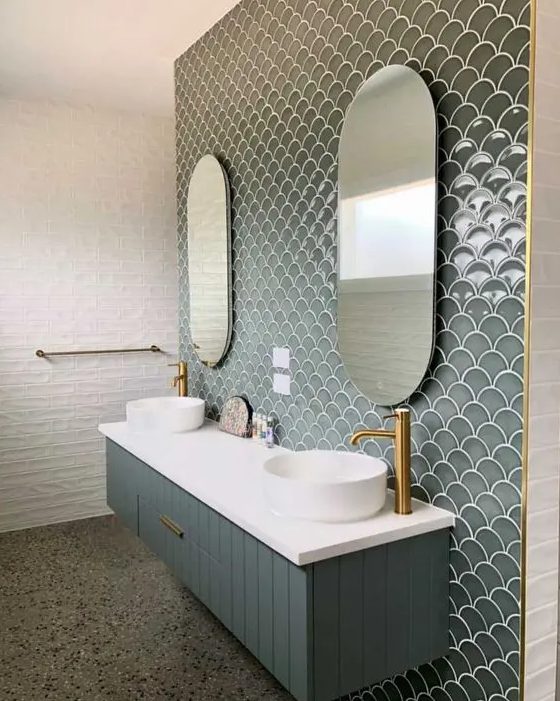 an eye catchy bathroom clad with white tiles and grey green fishscale tiles plus a matching vanity, sinks and gold fixtures