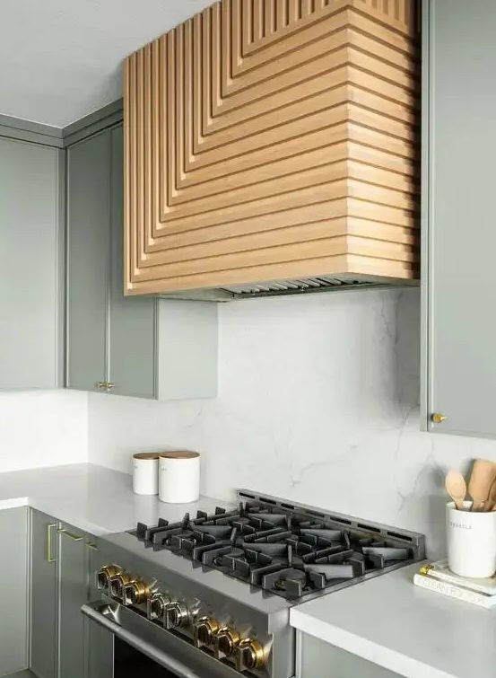 an olive green kitchen with white countertops and a backsplash plus a geometric wood clad hood over the cooker