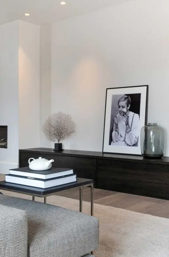 An ultra minimal living room with a dark stained storage unit, a grey sofa, a black table and a statement artwork
