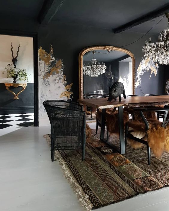 an unusual Goth dining room with soot walls and a ceiling, a living edge table, black chairs, a crystal chandelier and unique wall decor