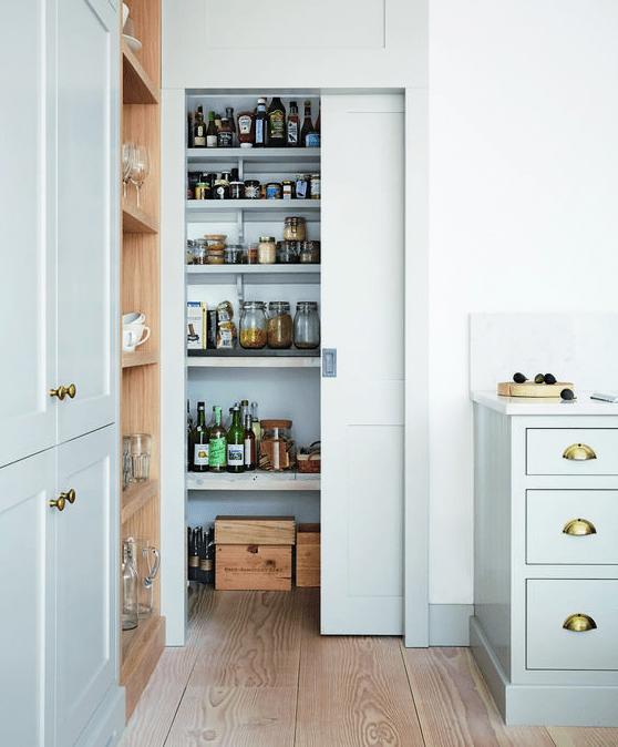 Kitchen with open door to the pantry larder cupboard, pale grey kitchen cupboards and wooden shelving.