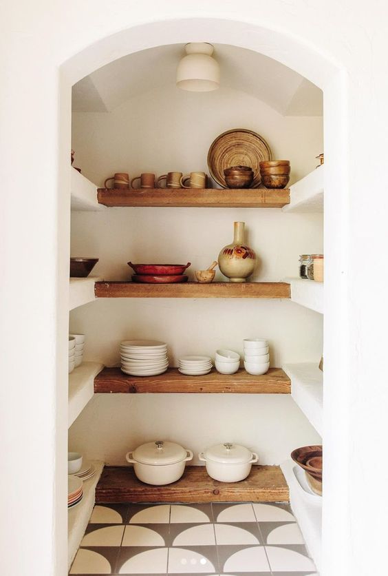 a beautiful Mediterranean walk in pantry with an arched entry, built in and stained shelves and lots of tableware and cookware