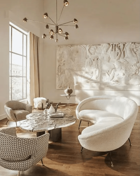 a beautiful and airy living room with unique decor on the wall, a white curved sofa and chairs, a curved coffee table