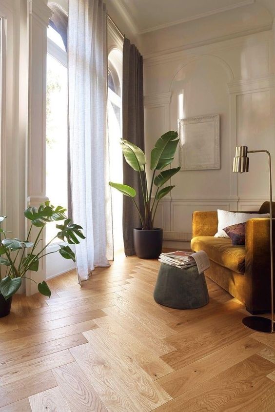 a beautiful contemporary space with molding, a mustard chair, a beautiful herringbone floor and some plants