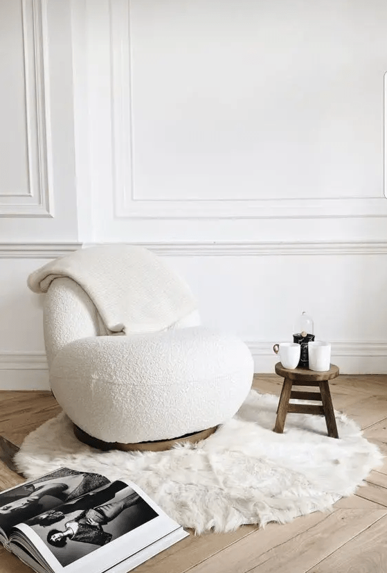a beautiful curved white boucle chair, a stained side table, a faux fur rug are a cool and trendy combo for a living room