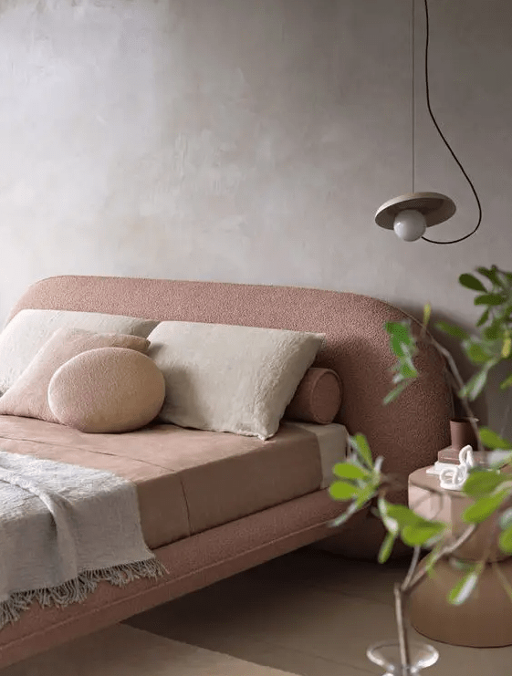 a beautiful pink curved bed with boucle upholstery and neutral bedding, a bedside table and a pendant lamp