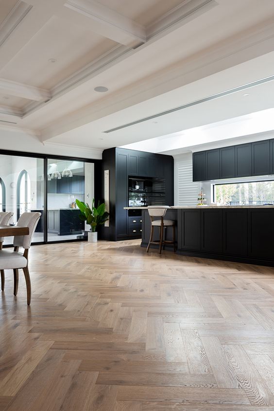 a black farmhouse kitchen with a herringbone floor, a window backsplash and a dining zone here is a stylish and chic space