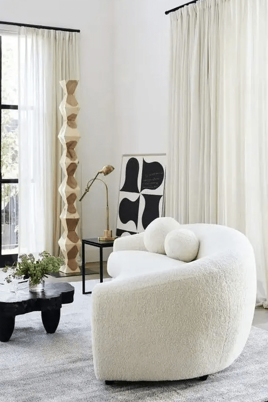 a chic contemporary living room with a creamy boucle sofa, a black table and some art, neutral drapes