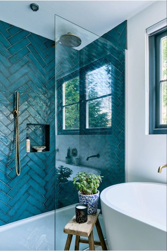 a coastal bathroom with a shower space done with blue herringbone tiles, an oval tub and a window for natural light