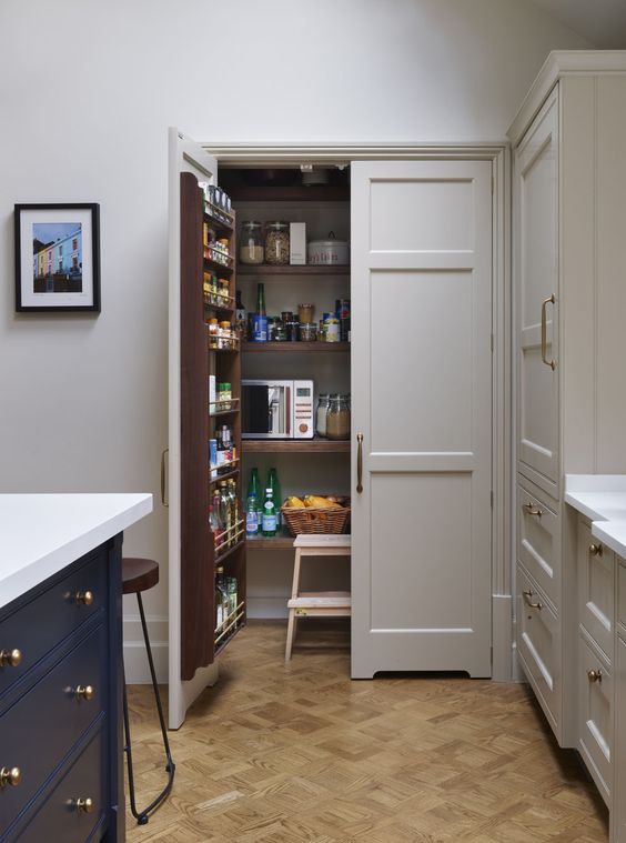 a cool and small pantry with shelves on the doors and inside it, with a stool and baskets for storage