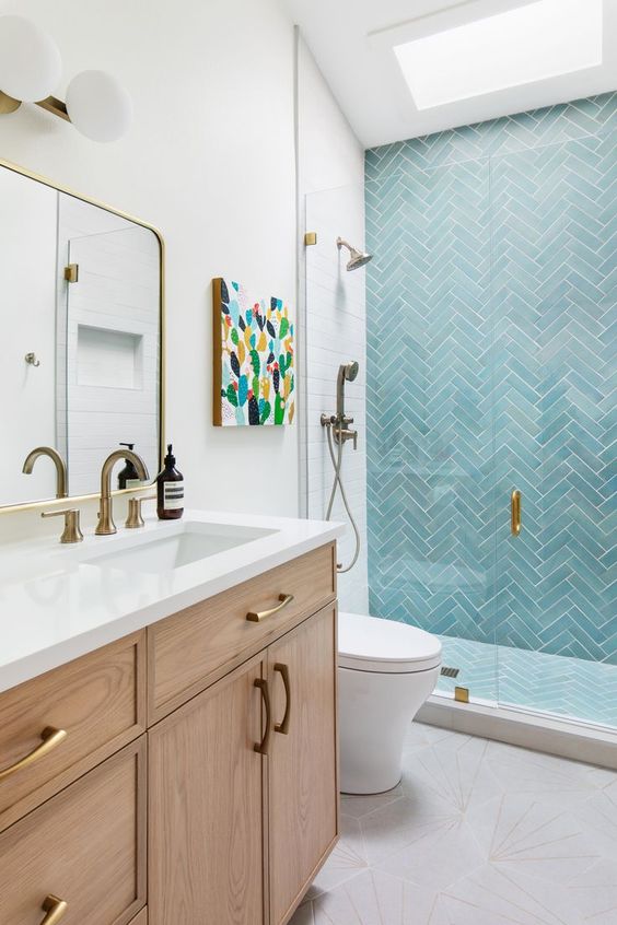 a cool modern bathroom with a skylight, a shower space with turquoise herringbone tiles, a stained vanity and brass fixtures