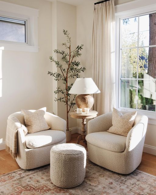 a cozy nook by the window with neutral boucle chairs, a pouf, a rug, a side table with a lamp and greenery is amazing