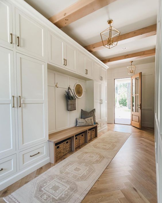 a creamy farmhouse mudroom with a herringbone floor, wooden beams and beautiful creamy cabinetry plus baskets