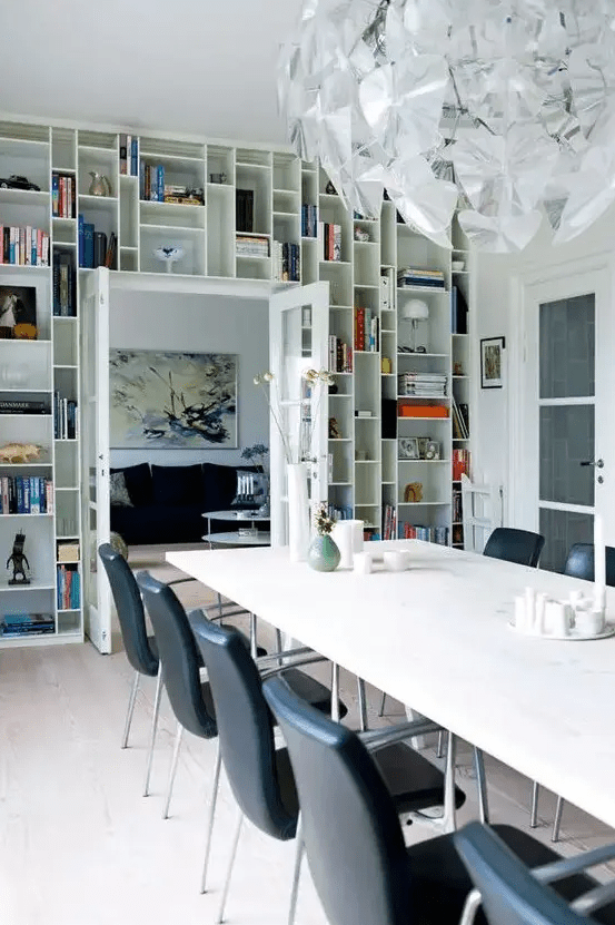 a dining room with a doorway wall taken by open shelves and displaying books, art and candleholders is a cool idea for saving space