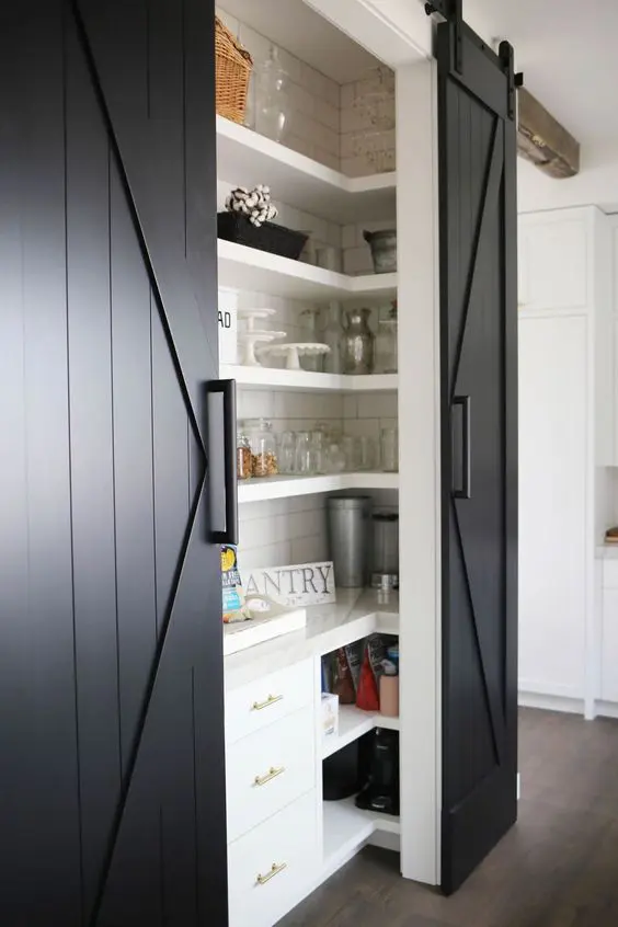 a farmhouse pantry with black barn doors, white shelving and some storage units is a cool space for any kitchen