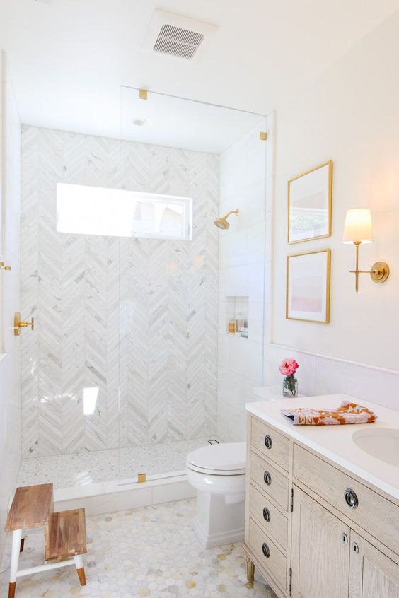 a glam white bathroom clad with marble herringbone tiles and hex ones, a whitewashed vanity and gold touches