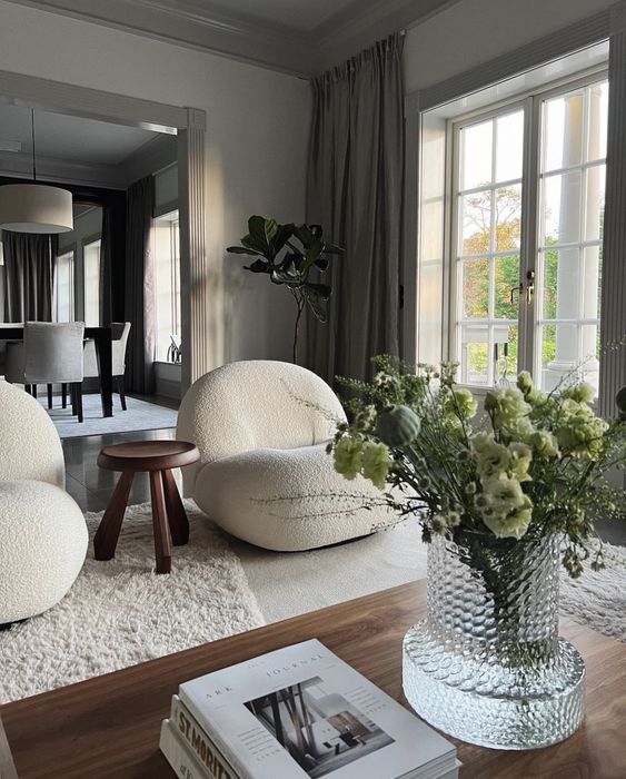 a grey living room with creamy boucle chairs, a neutral rug and a stained coffee table and greenery
