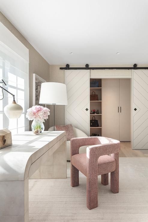 a large neutral cloffice with a waterfall desk, a pink boucle chair, a closet with barn doors is a cool and feminine space