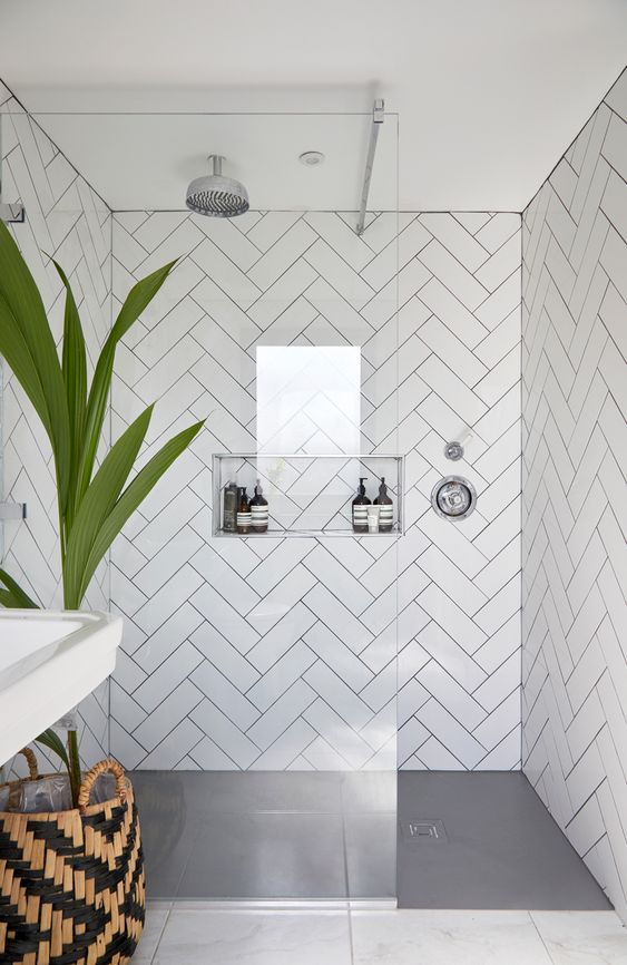 a large shower space clad with white herringbone tiles all over and a niche shelf for storage