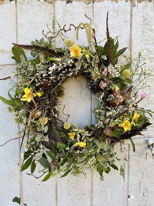 a messy and textural spring wreath with greenery, branches and twigs, yellow blooms, willow, feathers for a boho feel