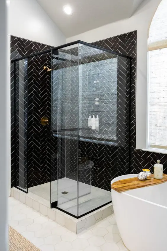 a modern bathroom with a shower space clad with blakc herringbone tiles, with a hex tile floor and an oval tub