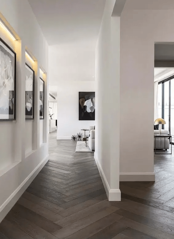 a modern exquisite space with white walls, a dark-stained herringbone floor, black and white artwork and some neutral furniture