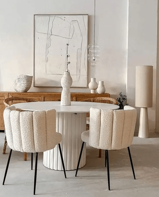 a neutral dining room with a light-stained credenza, a round table, creamy boucle chairs and a pendant lamp over the table