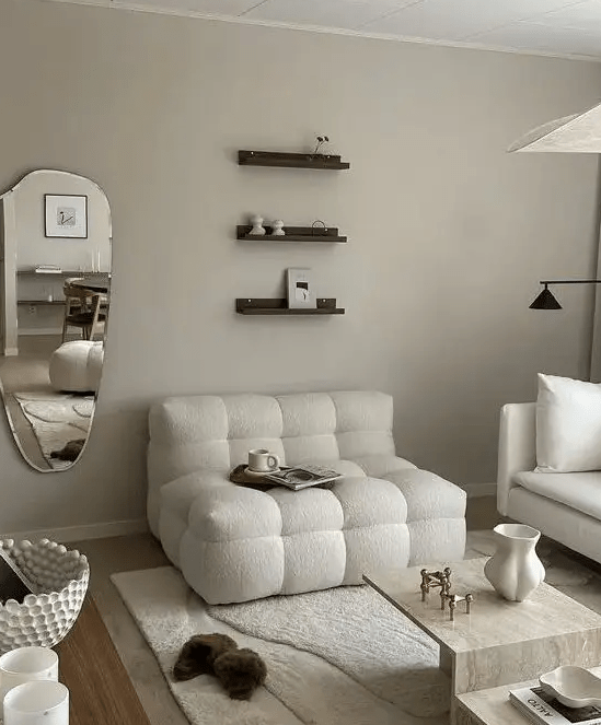 a neutral living room with white boucle seating furniture, a stone coffee table, small shelves and a mirror