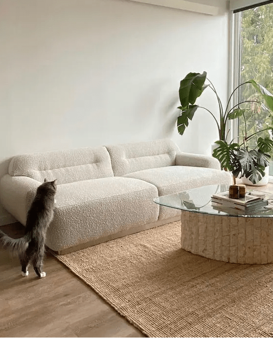 a neutral low boucle sofa, a textured rug, a table with a base made of cork and some greenery in planters for a trendy space