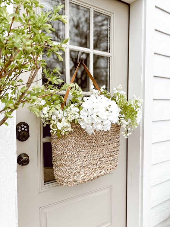 a pretty spring door decoration of a basket with greenery, white blooms is a cool farmhouse alternative to a wreath