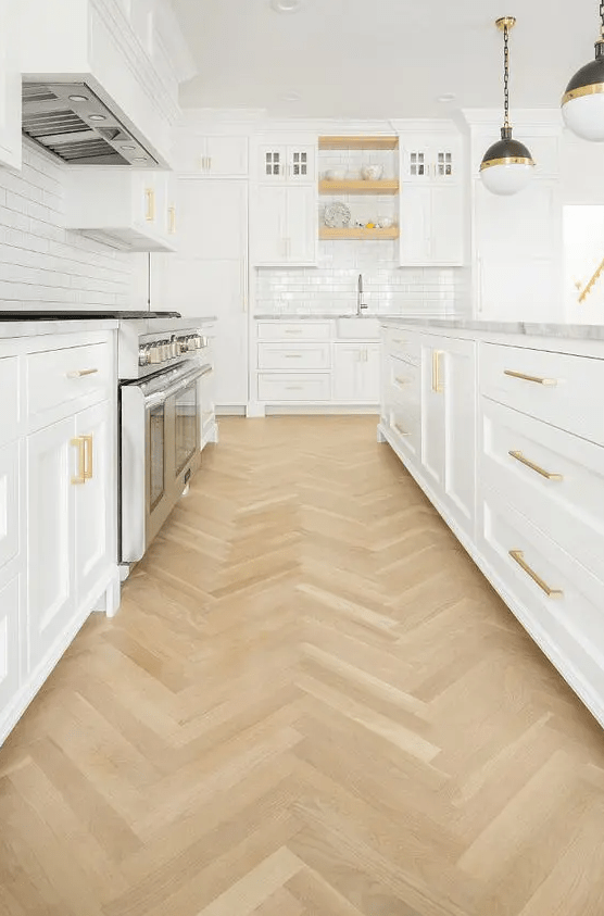 a pretty white modern farmhouse kitchen with shaker cabinets, a white subway tile backsplash, a herringbone floor and pendant lamps
