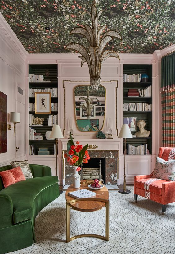 A quirky living room with a fireplace and blush and black built in shelves, a green curved sofa, a coral chair and a coffee table