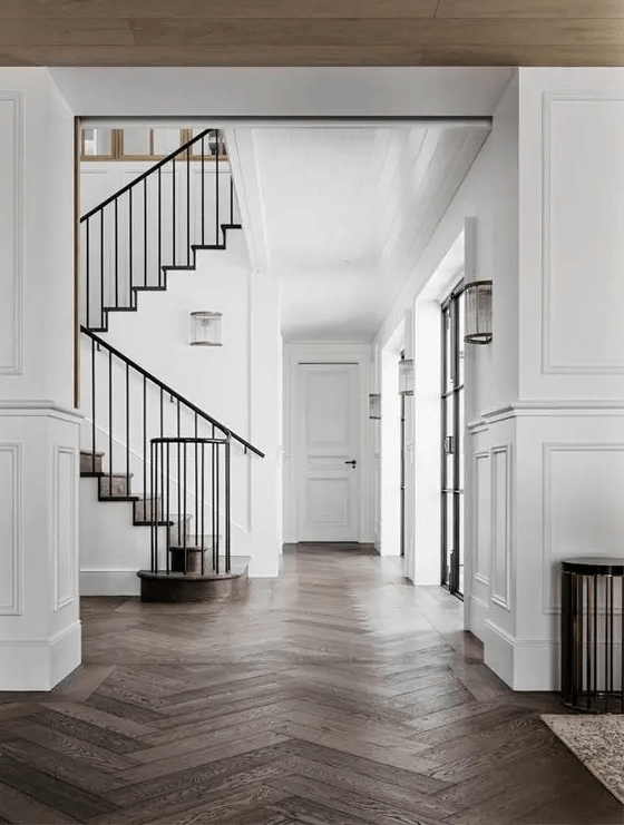 a refined space with white walls with molding and dark-stained herringbone floors, black railing is super chic