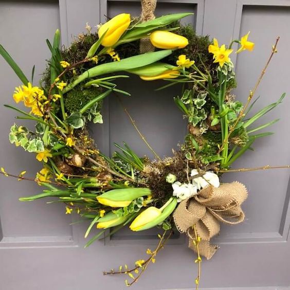 a rustic spring wreath with moss, greenery, yellow tulips and a burlap bow is a gorgeous decoration