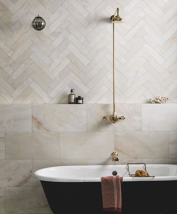 a serene bathroom done with herringbone and marble tiles, a black vintage tub and gold fixtures