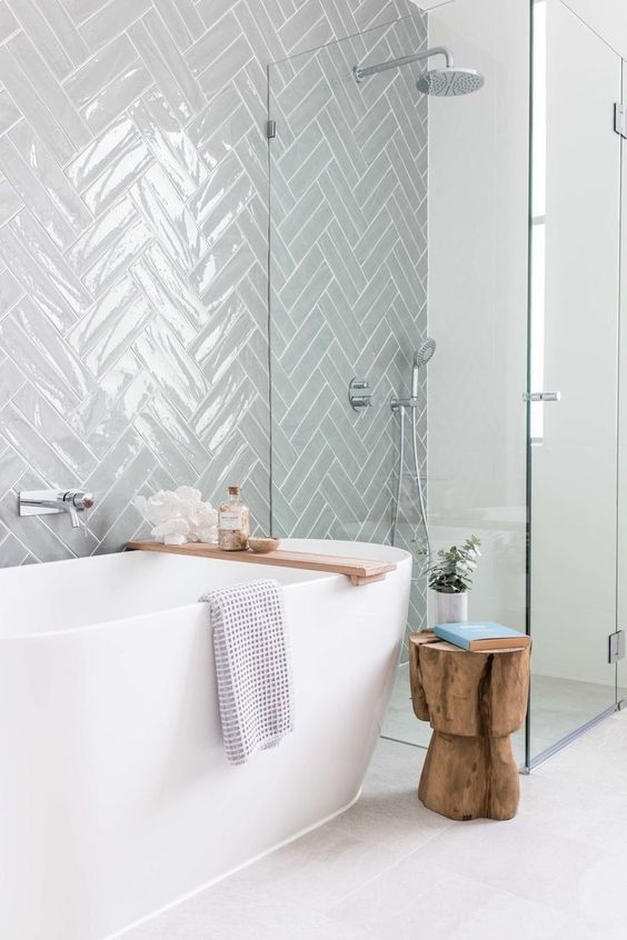 a serene contemporary bathroom clad with grey herringbone tiles, an oval tub, a shower space and a cork stool