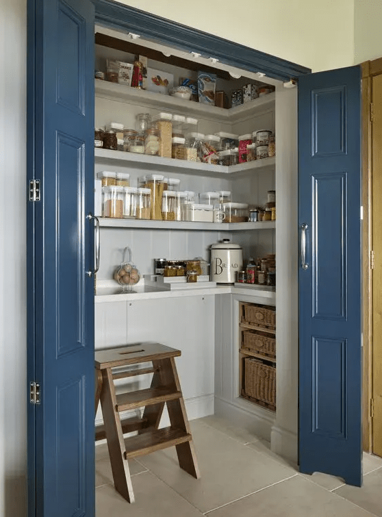 a small and chic pantry with built in cabinets, open shelves, baskets, a wooden stool and some jars is a super cool idea