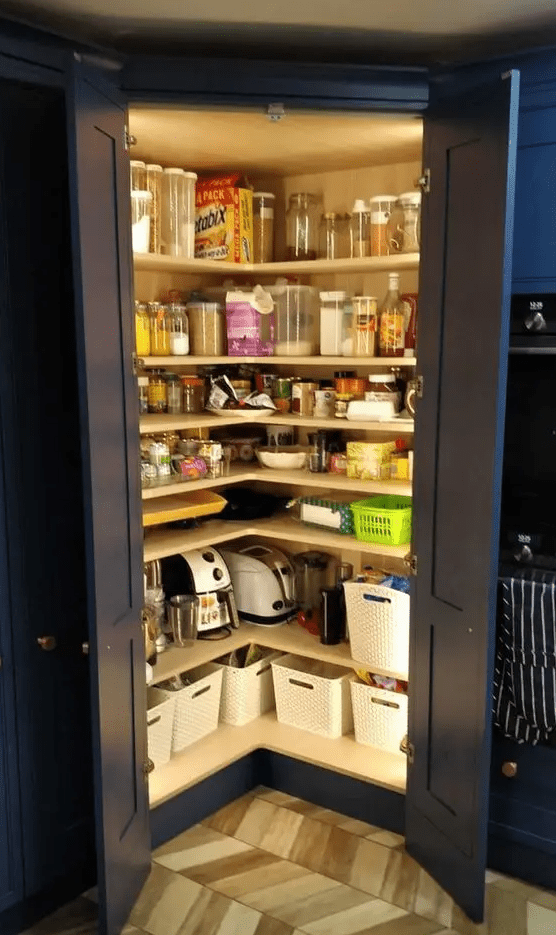a small pantry built in the kitchen, with navy doors, corner open shelves, cubbies and lots of jars and containers plus built in lights