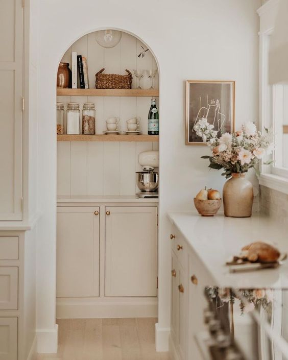 a small pantry with an arched entry, open shelves and blush cabinets is a smart storage space that loosk cohesive
