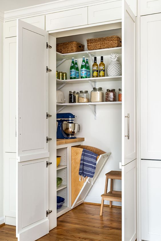 a small pantry with doors, open shelves, a single cabinet and lots of stuff and appliances stored inside