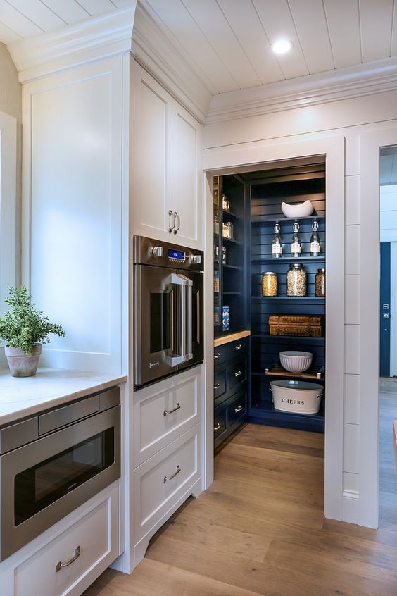 a small pantry with navy cabinetry and open shelves, with built-in lights and lots of stuff stored