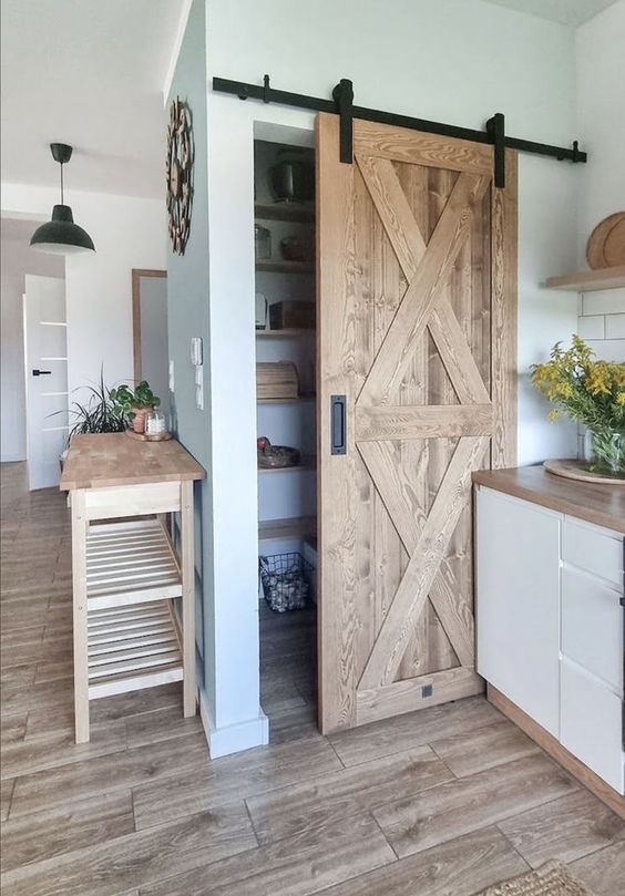 a small rustic pantry with a barn door, open shelves and some metal baskets is a perfect solution for a rustic kitchen