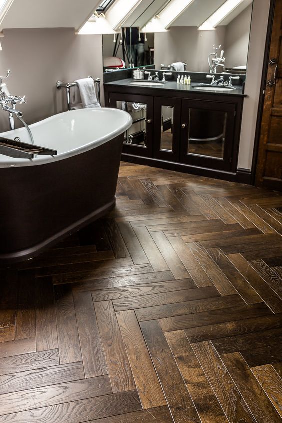 a sophisticated bathroom with grey walls, a herringbone tile floor, a black vanity and a black tub and a large mirror